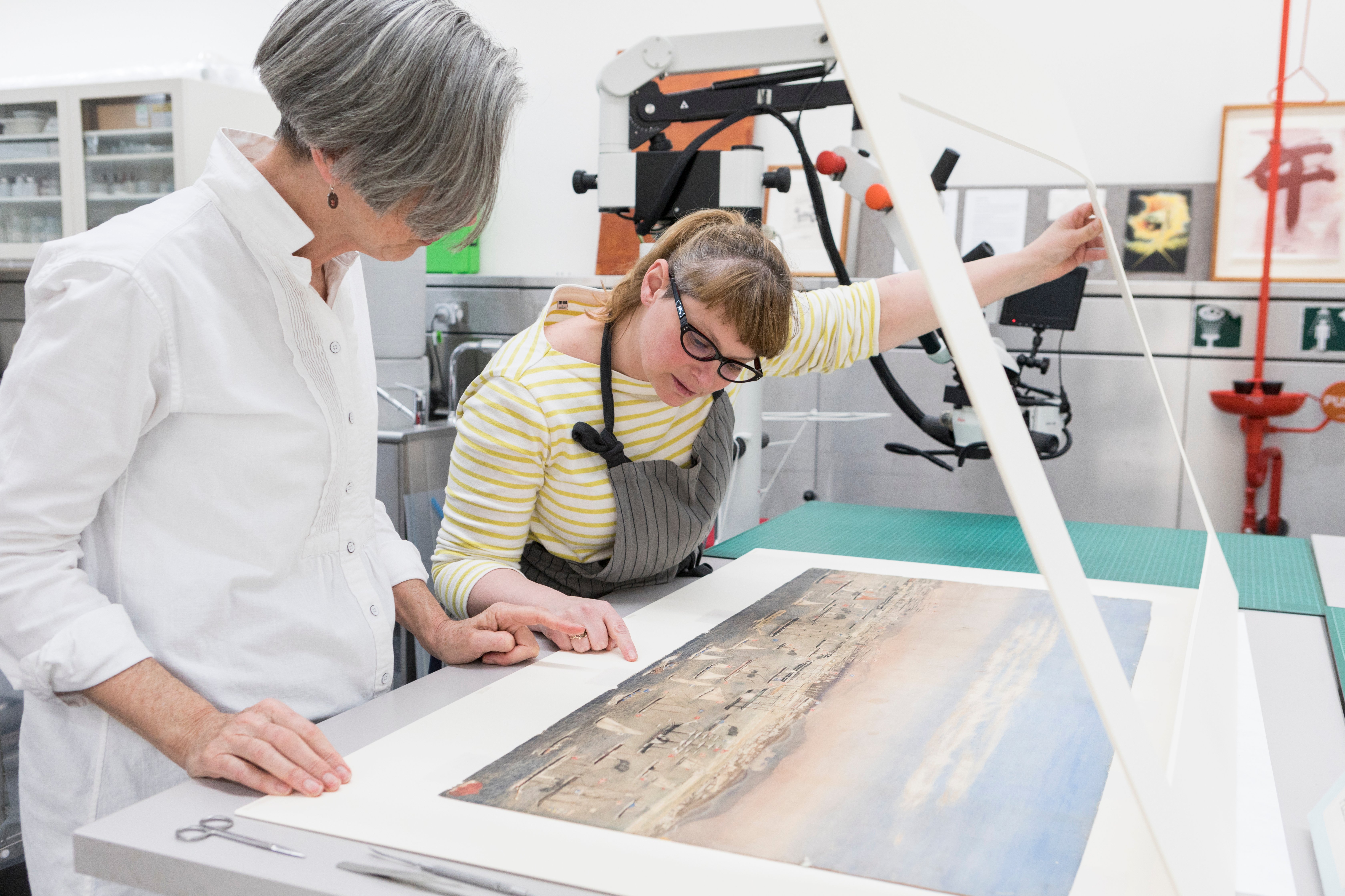 Two conservators working on View of the north shore, East Melbourne