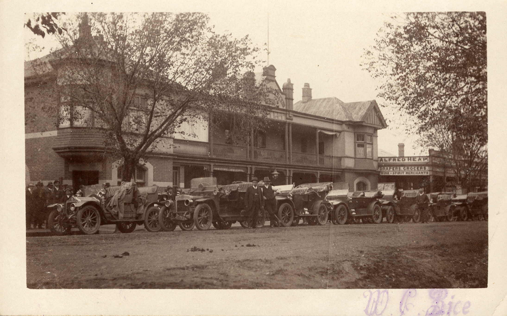 Shows row of cars outside Victoria Hotel, and Alfred Heap Drapers, Grocers, Wine and Spirit Merchants shop.