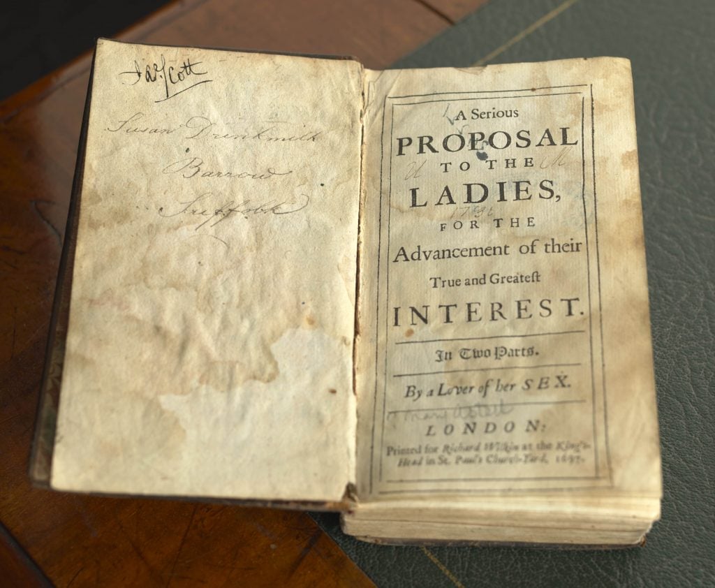 An open volume of Mary Astell's book 'A Serious Proposal to the Ladies, for the Advancement of their True and Greatest Interest', 1697, sits on a desk. 