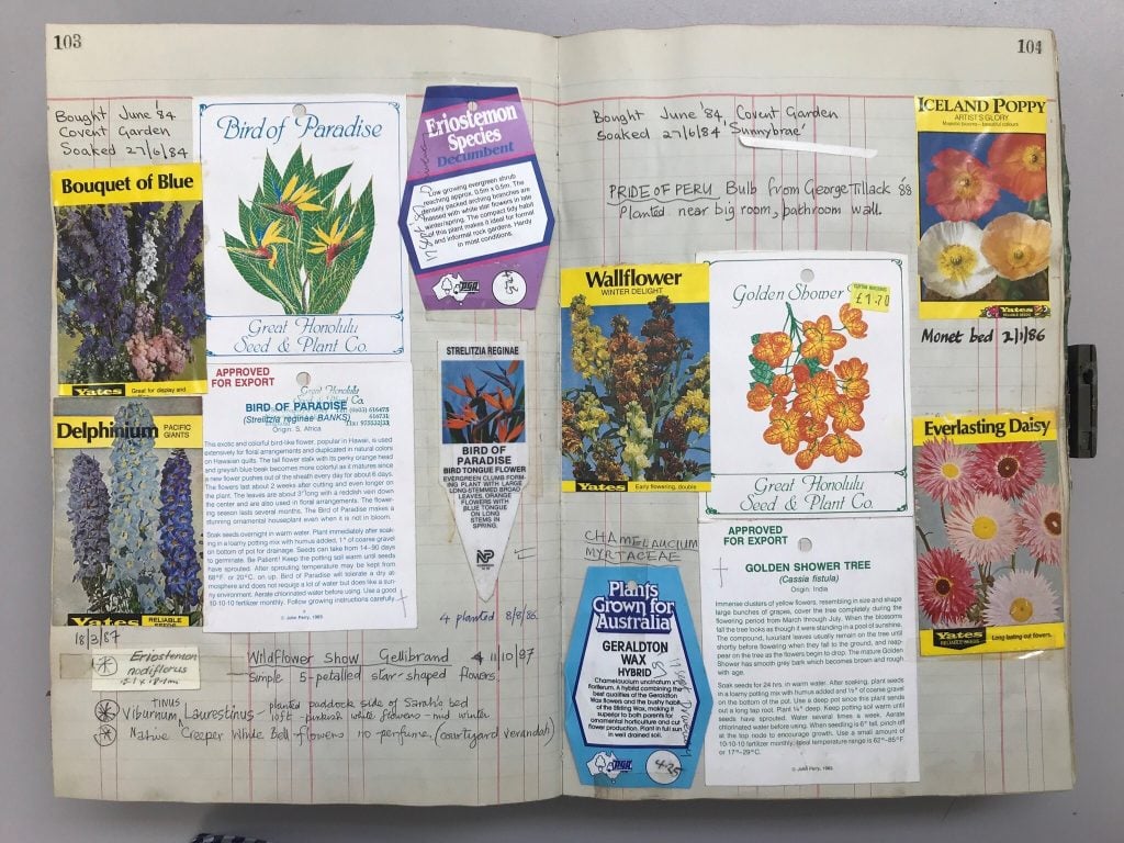 Colour photograph of a large ledger, opened to a set of pages depicting handwritten notes and various empty packets of seeds for plants and flowers.