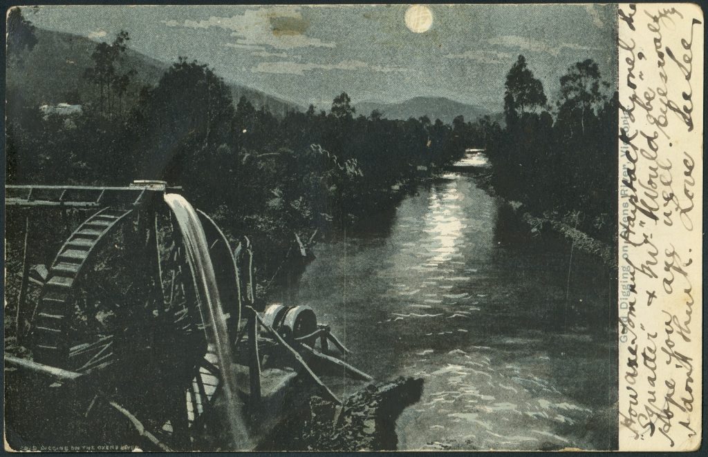 Postcard, Water wheel on the river, moonlit scene with mountains and trees in the background.