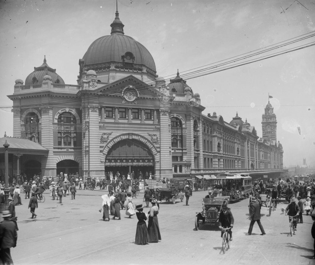 Flinders Street station, pedistrians , cyclists, trams and cars all around.
