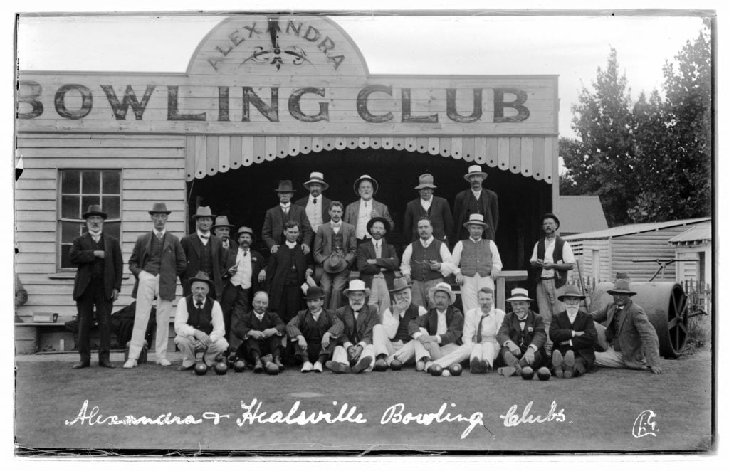group photograph of men members of the bowling club in front of the club building, a large roller on the right hand side of the picture