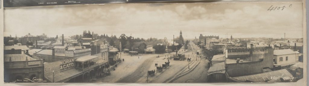 Panoramic view of  streets in the center of Bendigo, with horses and buggies, pedestrians, treetops in the park