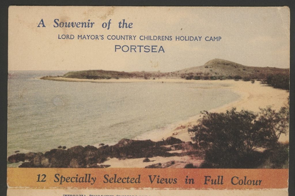 Souvenir colour  postcard of the Lord Mayor's Country Childrens Holiday Camp, Portsea. A long beach curves around the sea. Trees and rocks stand in the foreground, hills and trees in the background.. 