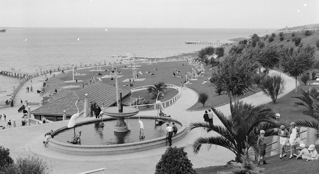 View looking out to the water showing a fountain, kiosk and children's playground. 