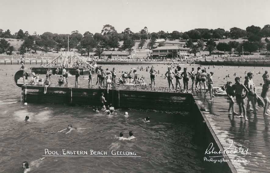 View from the promenade across the swimming enclosure. People swimming. One boy balancing on the treadmill wheel. 