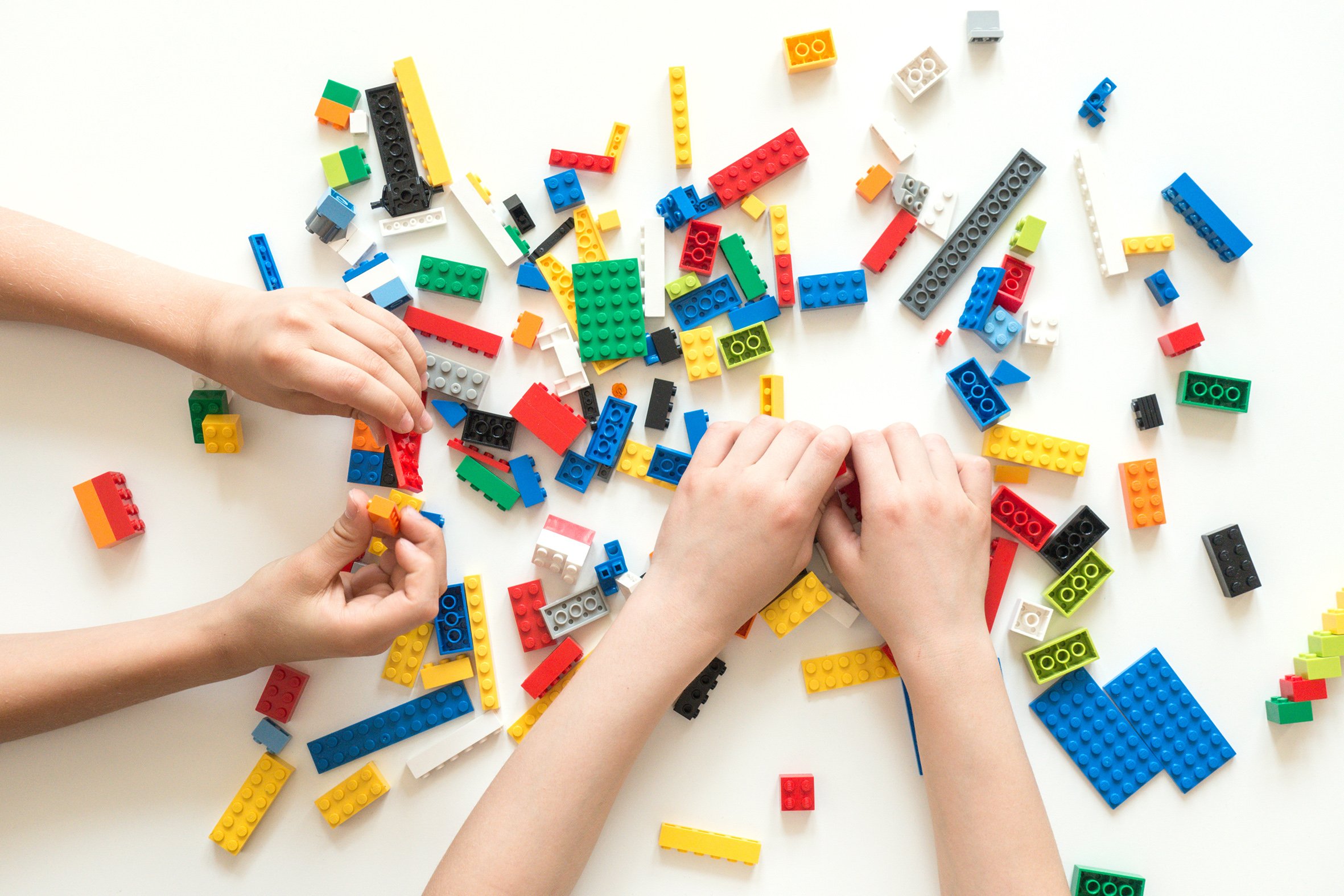 Children's hands are pictureed playing with colourful Lego blocks on a white table