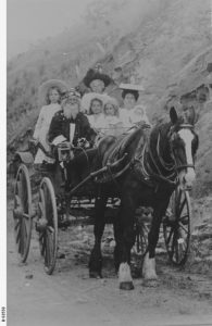 Black and white photo of a man dressed as Santa driving a horse drawn buggy accompanied by women and children 