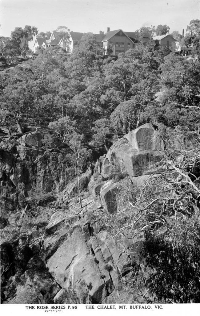 Photo of Mount Buffalo Chalet surrounded by dense trees. Large rocks in the foreground. 