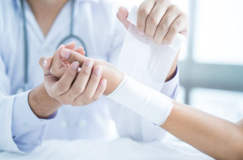 Close up view of a doctor wrapping a white bandage around a patient's wrist.