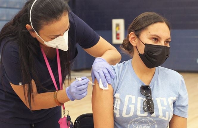 Nurse administering vaccine injection to woman. Both people are wearing masks.