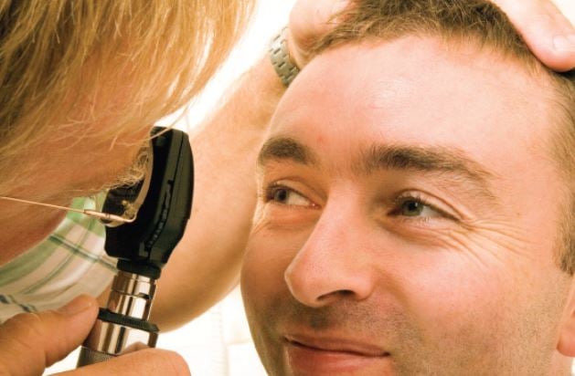 Close up of a man's face smiling, looking into an opthalmoscope held by a doctor examining his eyes.