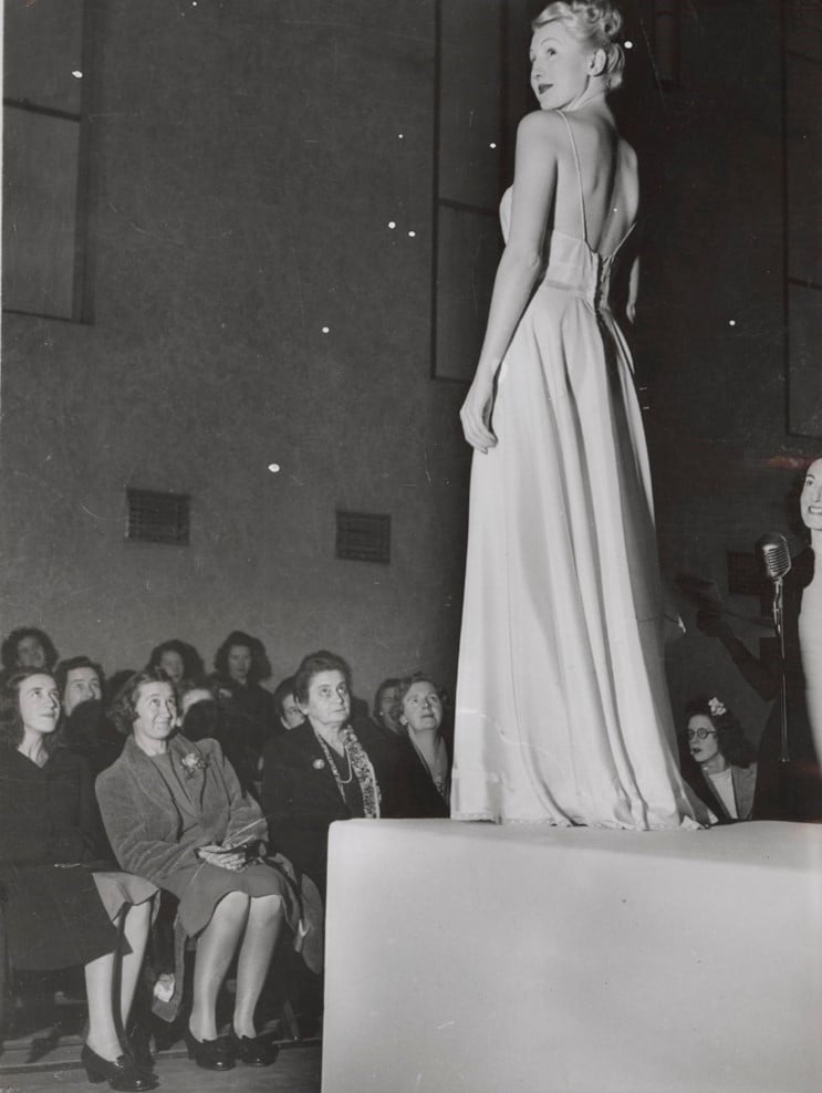 A woman on a podium wearing an evening gown in front of a female audience
