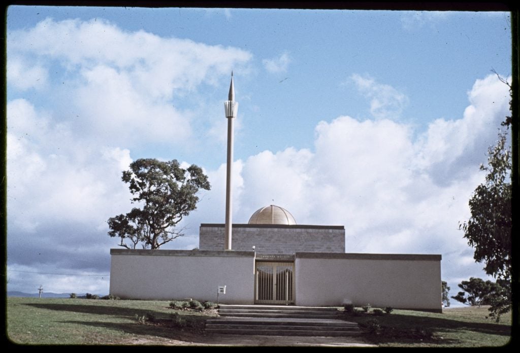 photograph of mosque with a golden donme and minaret on a tall spire. some gum trees around the building