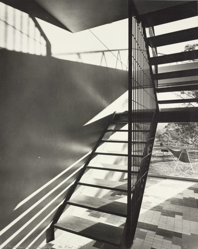 photograph of return interior staircase, with open treads letting light through, view to outside with a metal garden chair behind.