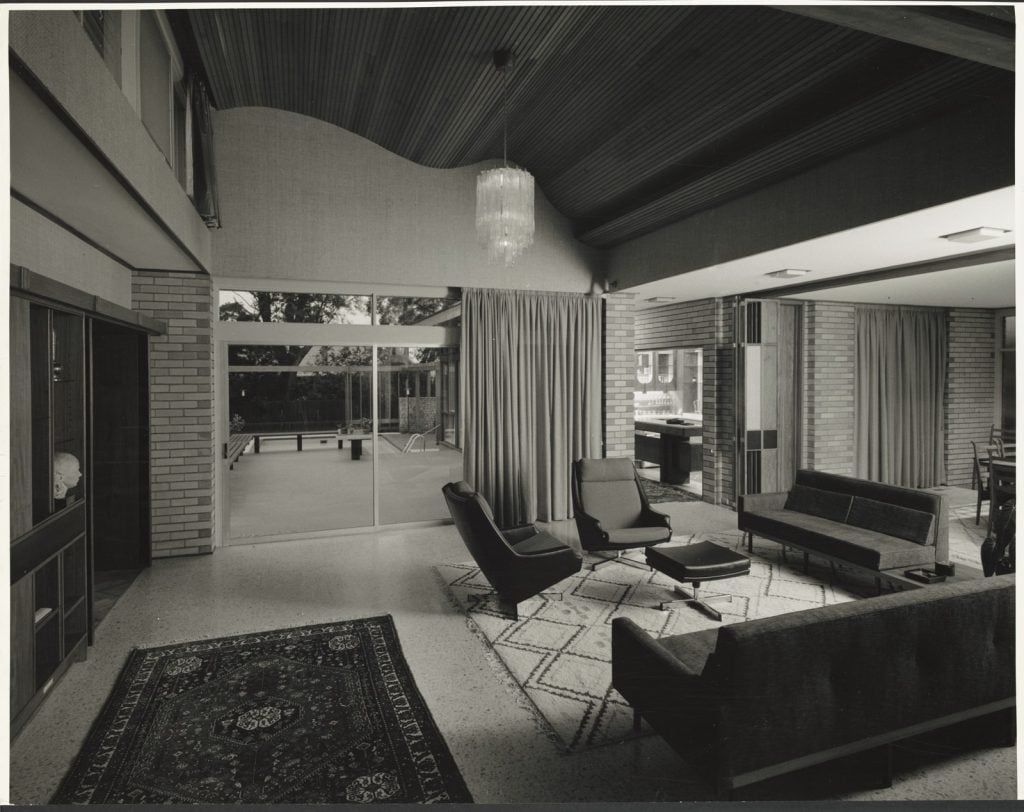 photograph of interior of house, curved timber ceiling, entry way looking through to outdoor paved area, lounge suite to the right foreground