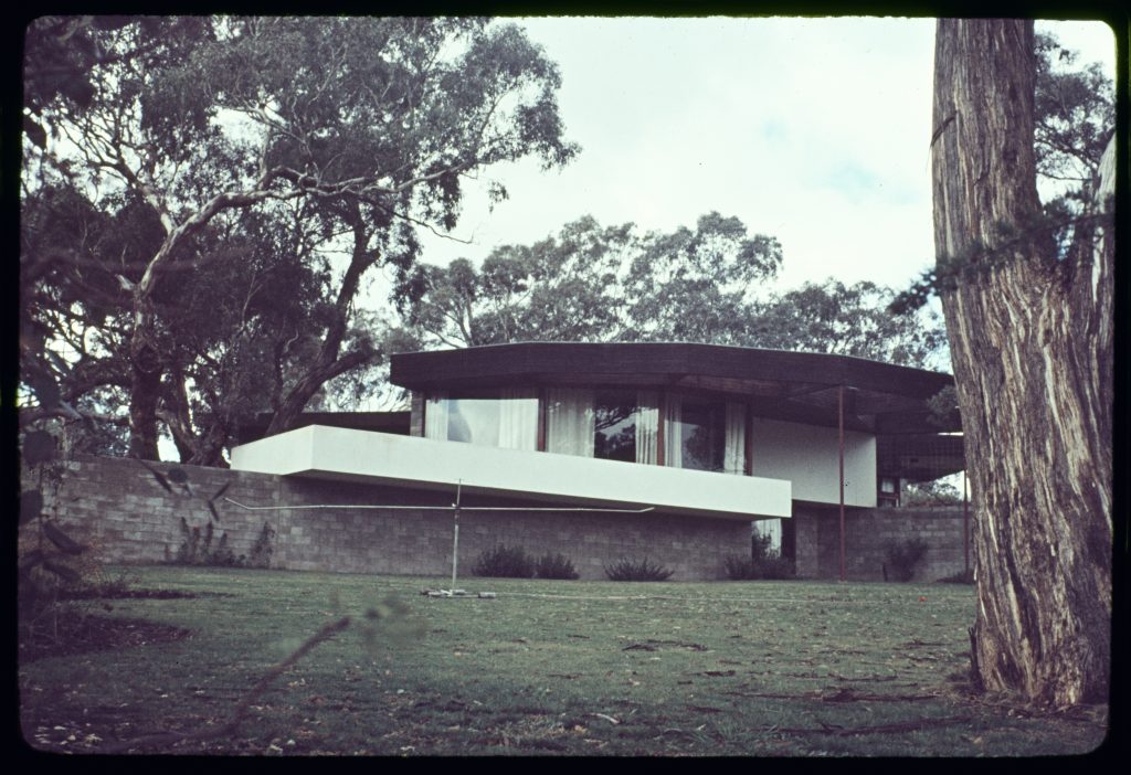 photograph of house - curved main structure flanked by brick walls, surrounded by gum trees.
