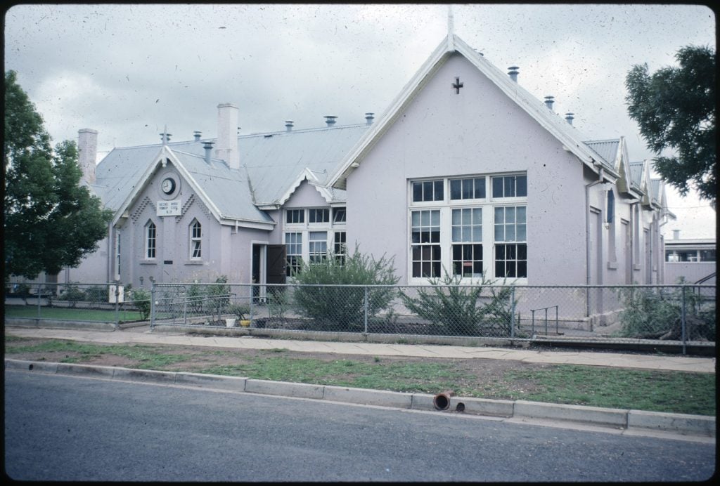 Exterior views of single storey classrooms, painted pink, with gabled roof. The school was the first state primary school in Victoria.