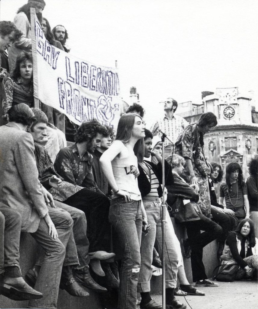Black and white photo of protestors at a gay liberation demonstration. There is a protest banner in the background.
