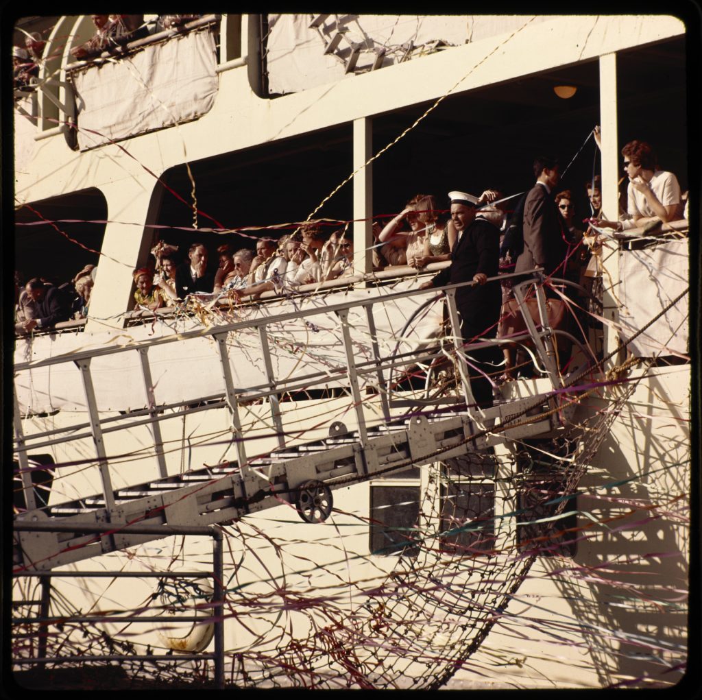 photograph of a ship with passengers, streamers and the gangplank lowered.
