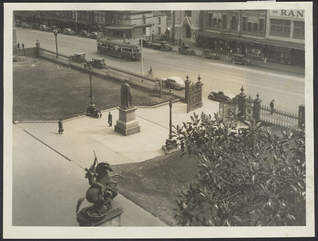Sepia image of view from the terrace of State Library of Victoria after the removal of trees on the south lawn, November 1938. Shows the main central steps of the Library and the bronze statue of St George and the dragon.