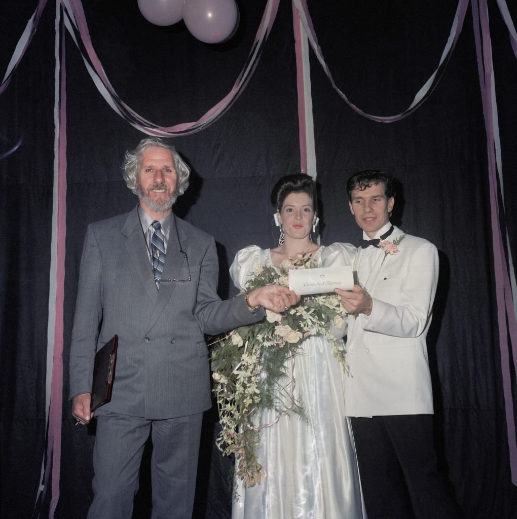Three-quarter length image of a wedding celebrant handing a marriage certificate to bride and groom. 