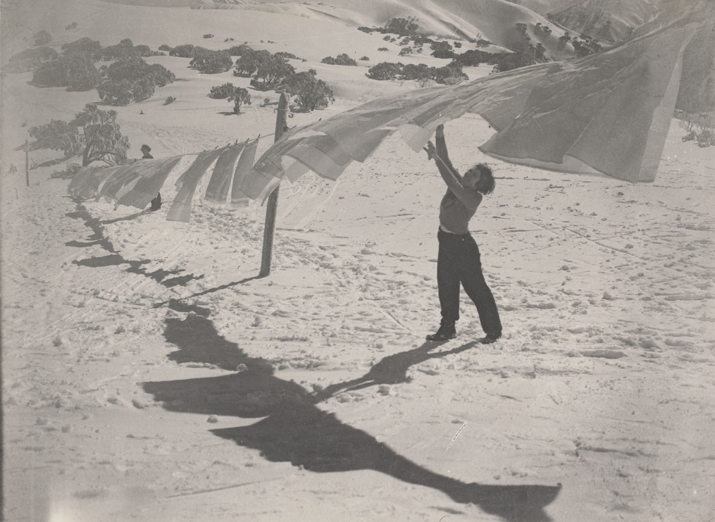 Woman at a washing line, on a sunny and windy day, with snow covered surrounds.