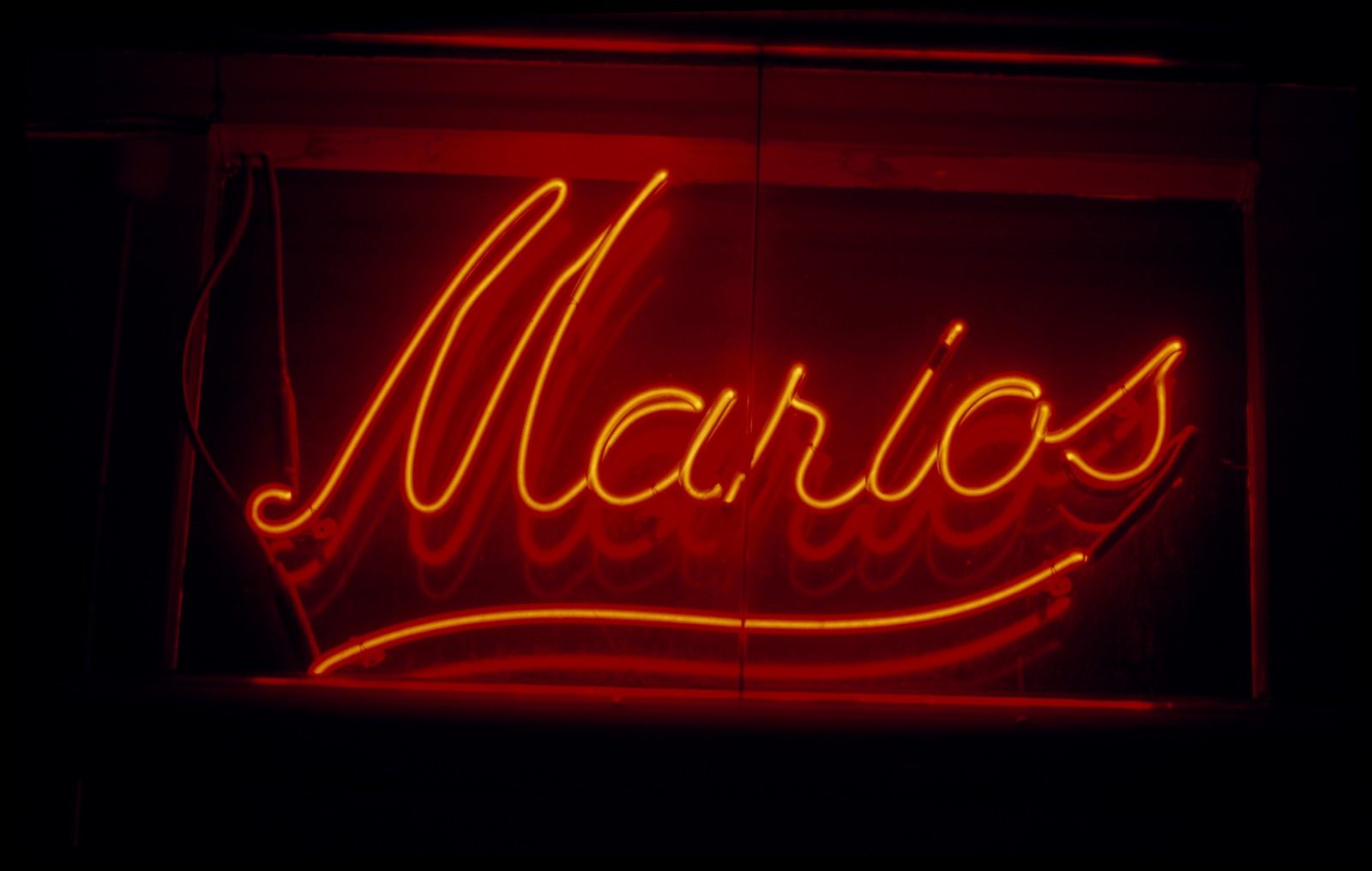 Photo of red neon 'Marios' sign in flowing cursive script. 