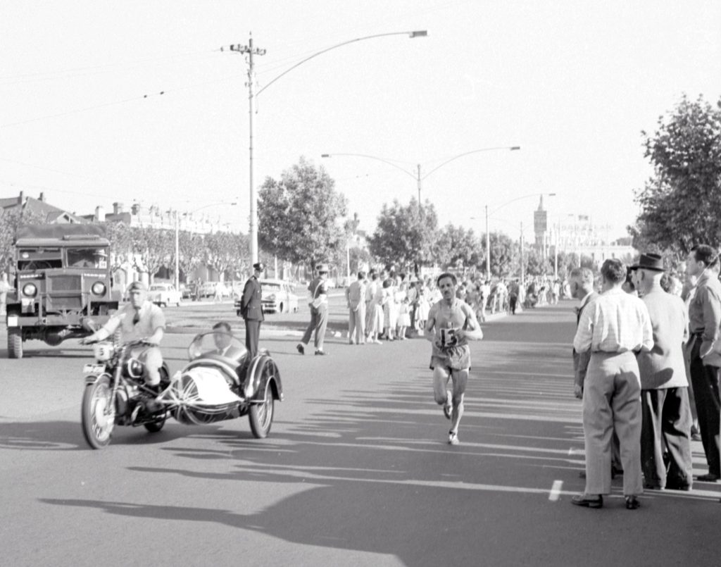 Photograph of Alain Mimoun running on his own with a motocycle and side car next to him.