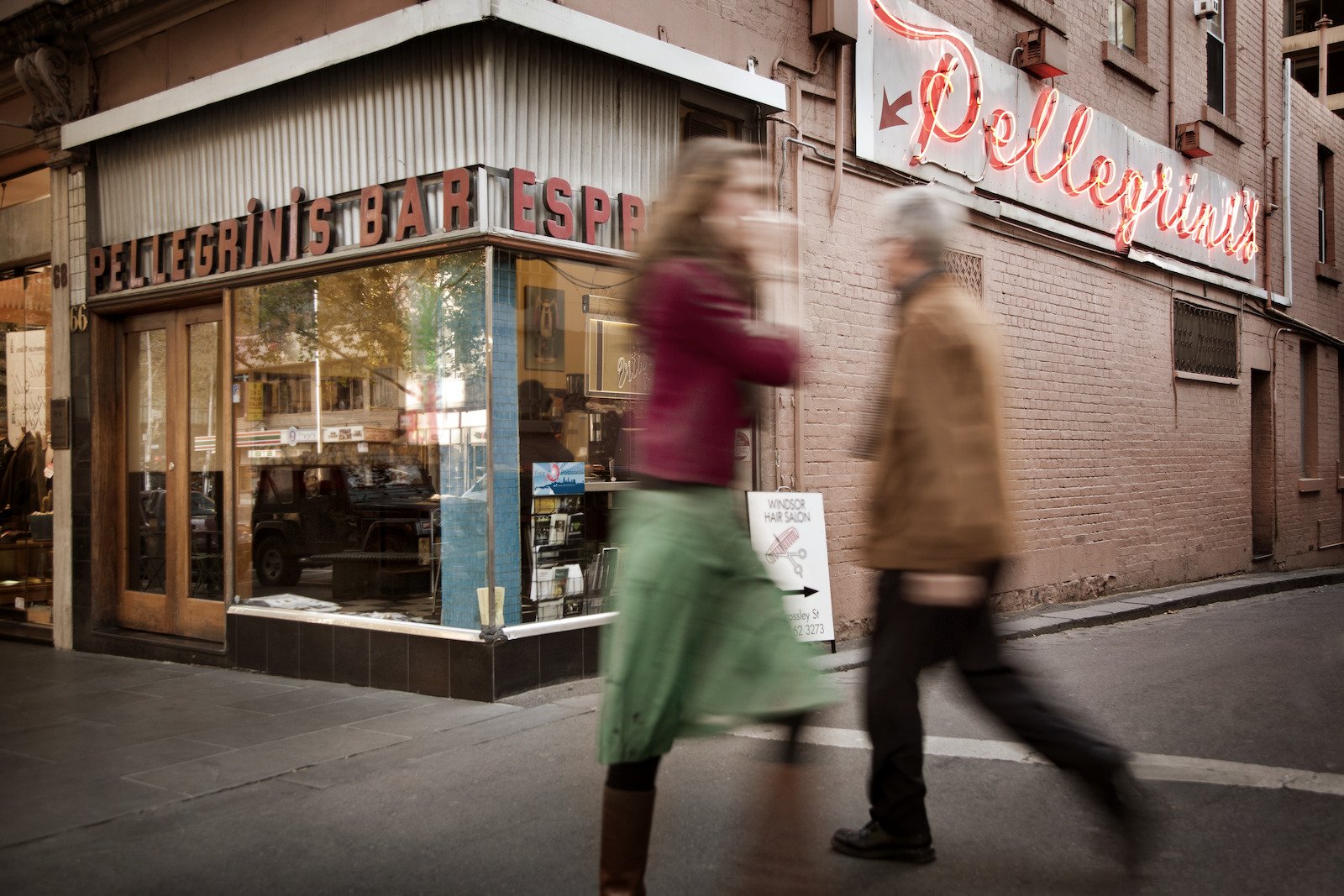 Exterior of Pellegrinis bar with visibler neon signage, pedestrians walk past in foreground