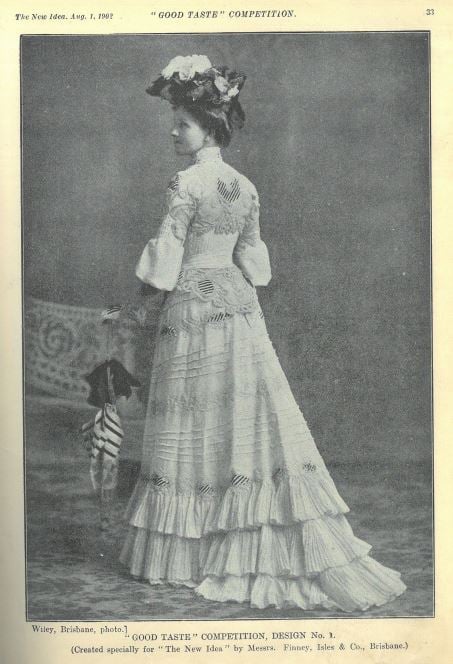 Black and white photo of woman in long flowing white dress and matching hat. 