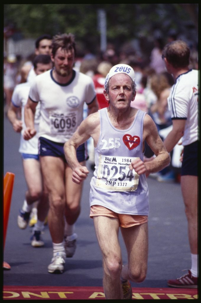 Photograph of an older man in a singlet running.