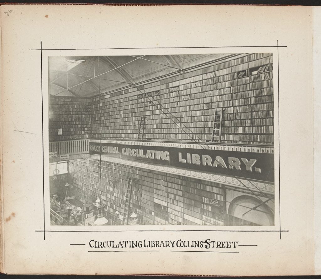 Black and white photograph showing two stories of book shelves with ladders, with sign reading ‘Cole’s Central Circulating Library’.