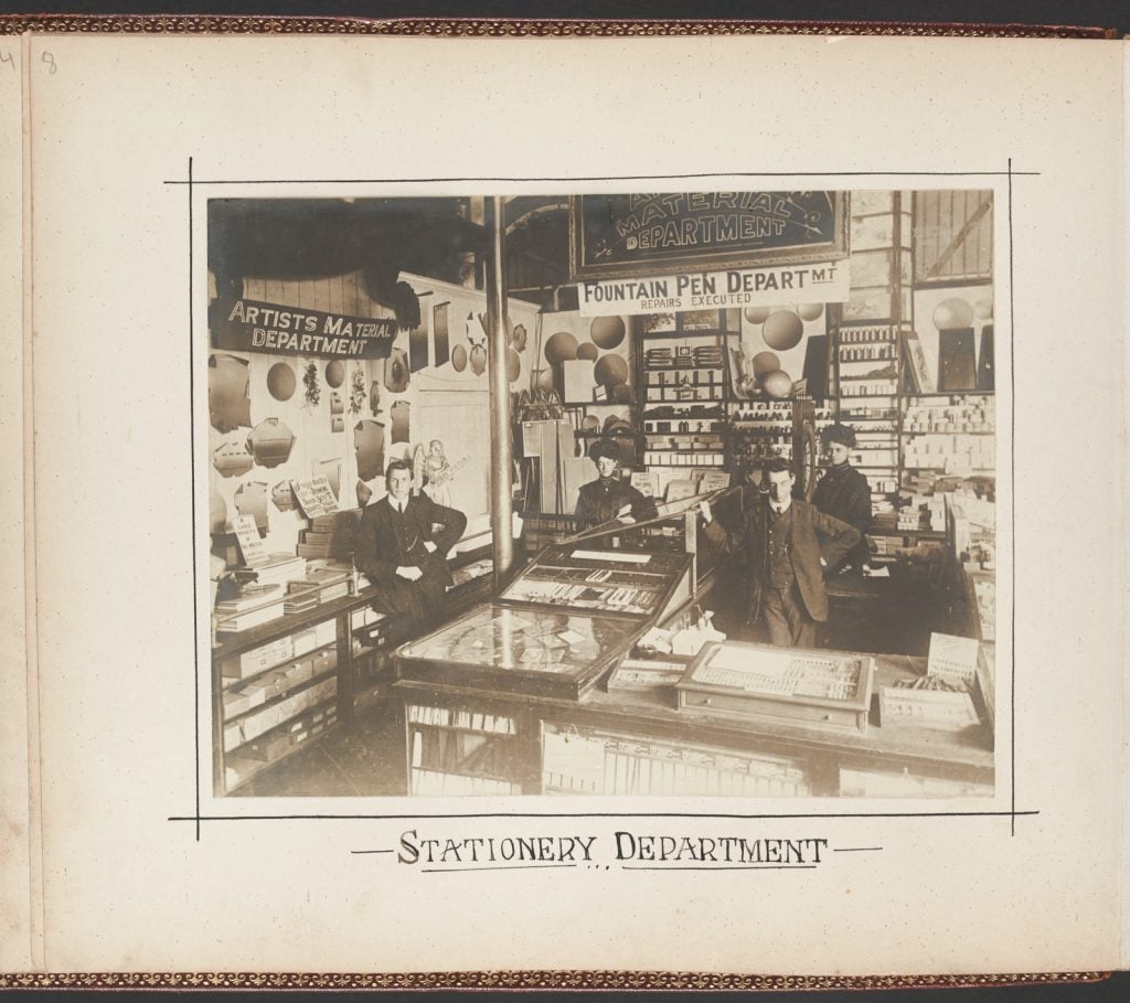 Black and white photograph showing staff at their counters in the stationery department.
