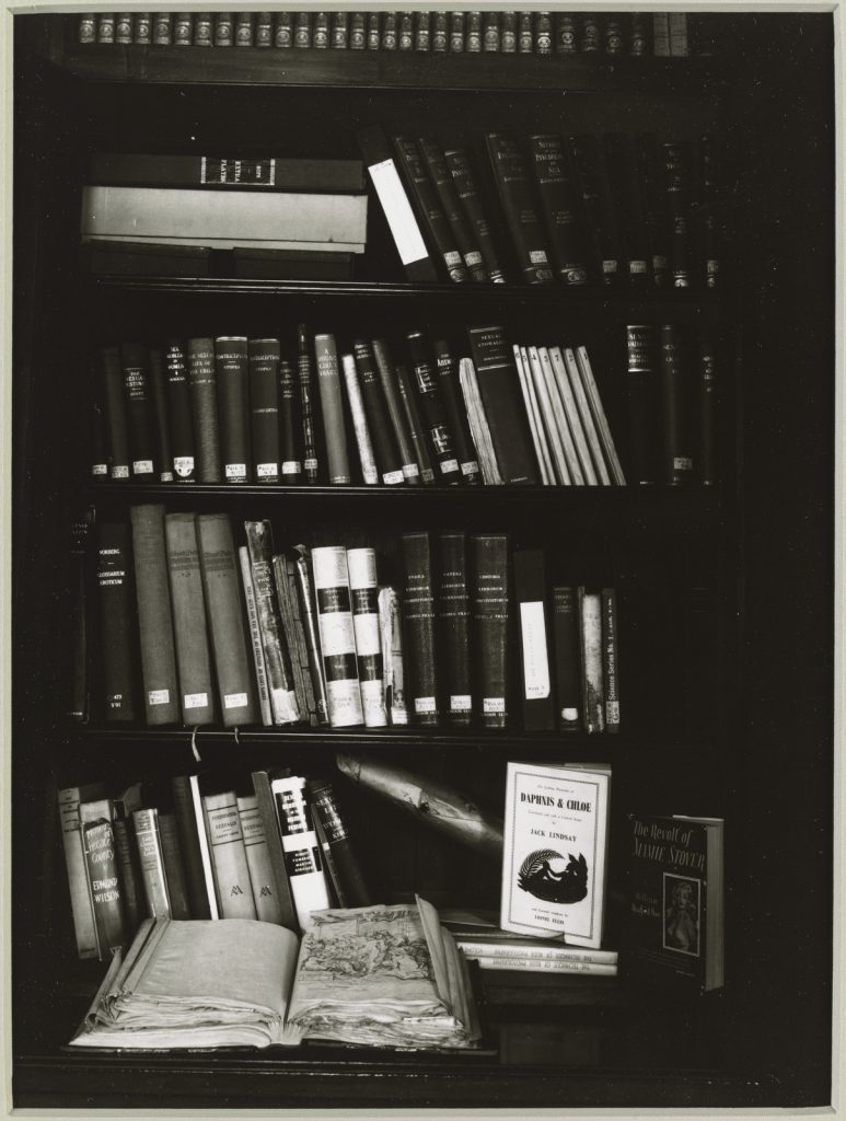 Books in the old office of the Principal Librarian, State Library of Victoria. Rows of books on a bookshelf with an open book on the desk beneath