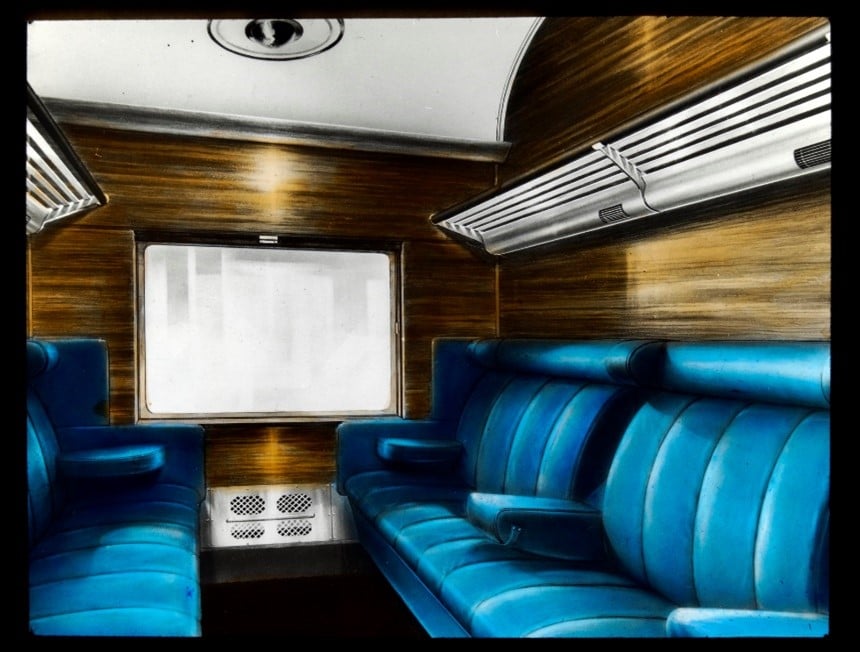 The inside of a train carriage with wood paneled walls and plush blue seats