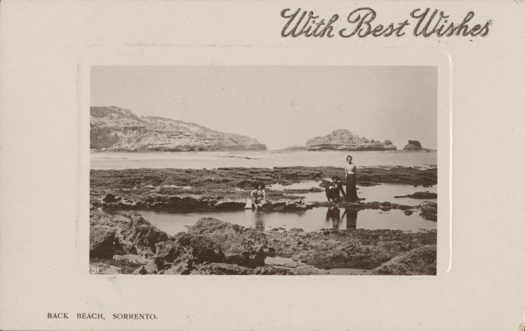 Man, woman and child standing on a rocky shoreline next to a shallow rockpool with the sea behind them. 