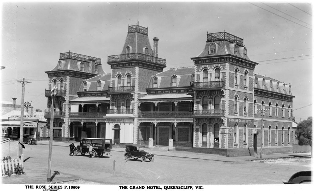 Grand three story hotel with old cards on the street in front. 