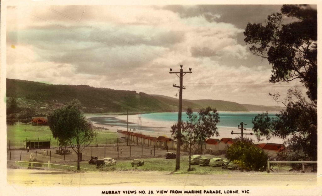 Stretch of coastline, with wooden bathing boxes in the foreground. 