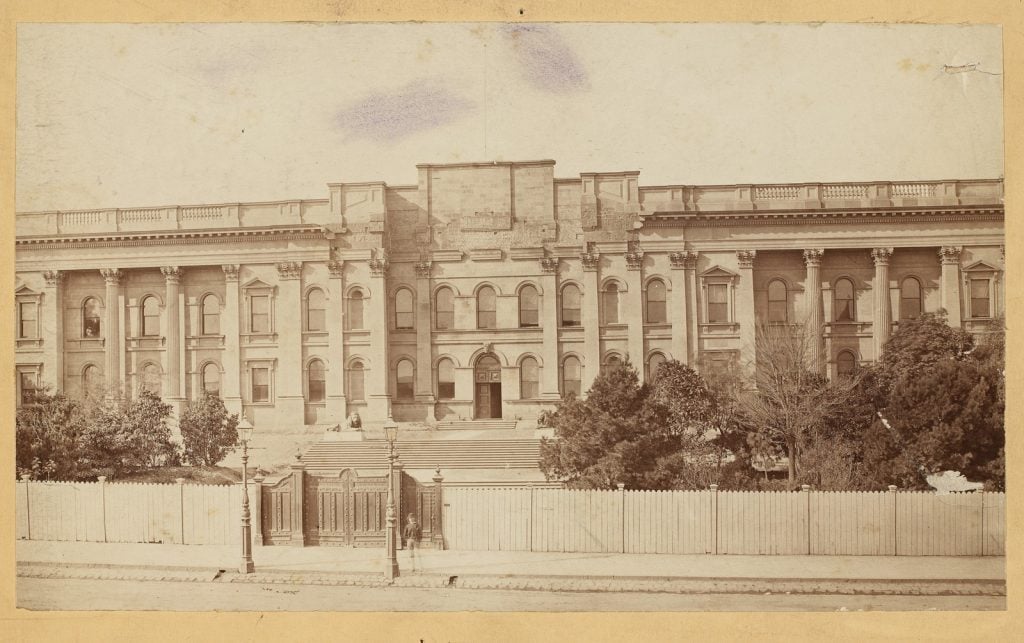 View from Swanston street of Melbourne Public Library (now the State Library of Victoria) with wooden fence and gates.