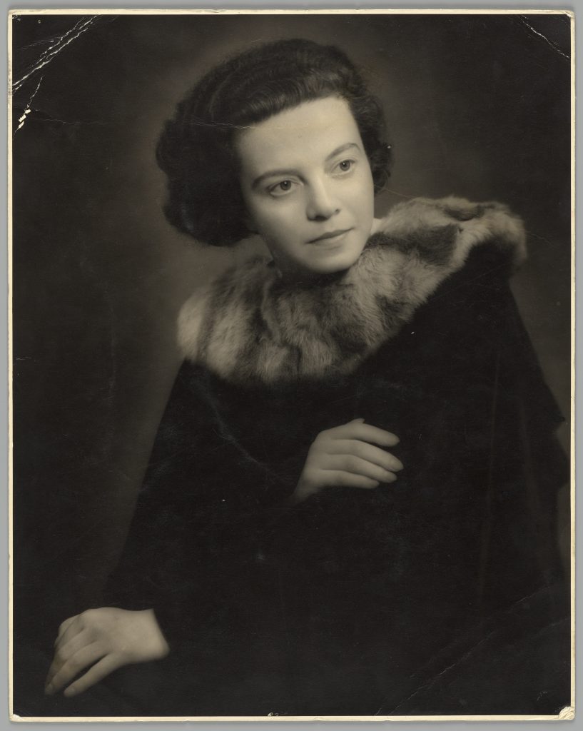 Black and white studio portrait of Sonia Revid, to waist, wearing fur coat. 