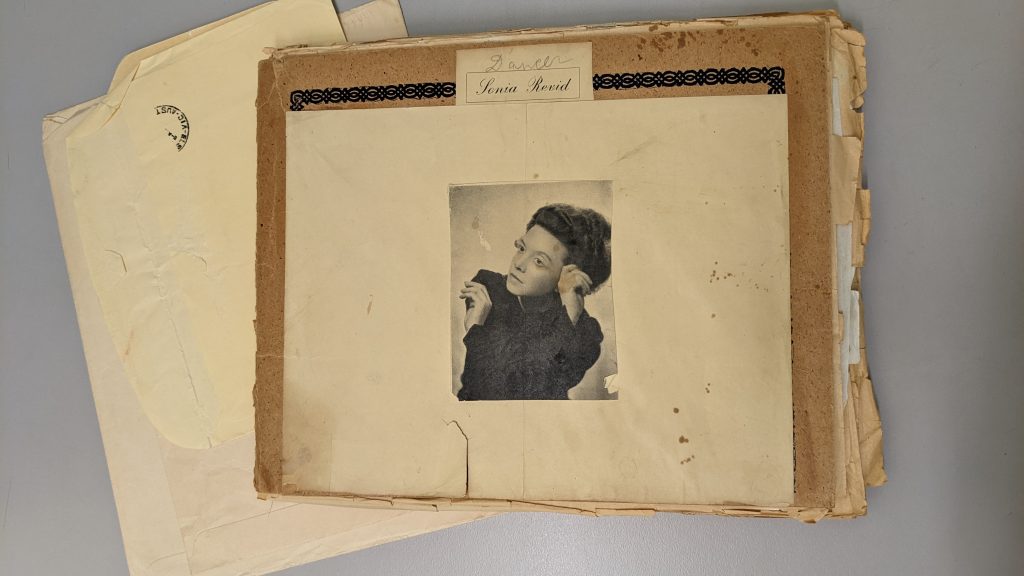 Photograph of scrapbook with studio portrait of Sonia Revid, from waist, affixed to front. Heading on cover of scrapbook reads "Dancer, Sonia Revid"