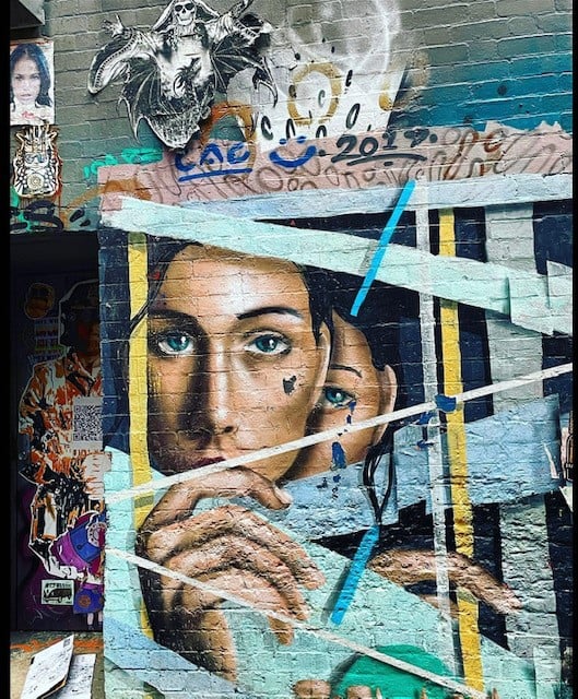 A mural on a brick wall of two female faces behind turquoise and yellow bars