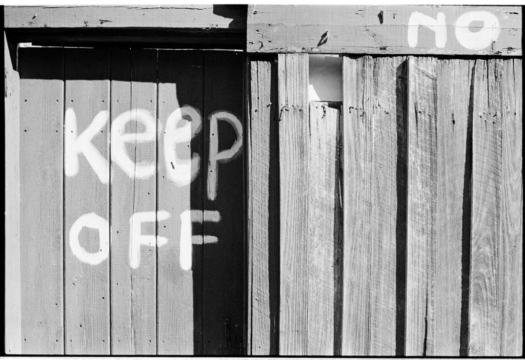 A photograph of a backyard wooden fence with "KEEP OFF" painted in white