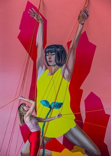 A blonde woman standing in front of a pink and red mural of a woman in a yellow dress