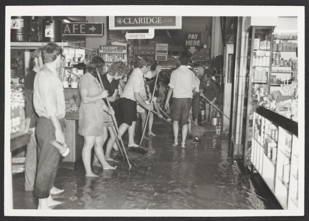 Barefoot staff using brooms to push the flood waters of out Coles Bourke Street Melbourne Store sometime in the 1960s or 1970s