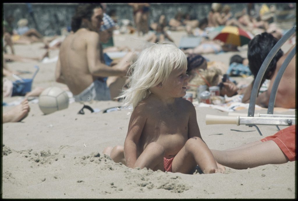 Small blonde child sitting in the sand at the beach.