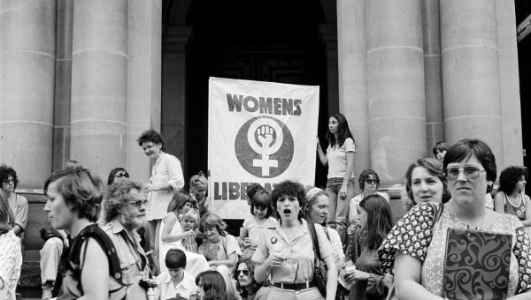 Black and white photograph of women in front of large banner reading 'Womens Liberation'