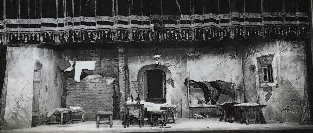 Stage set showing a run-down room with two windows, an exposed brick wall and some washing hanging on a clothesline. 